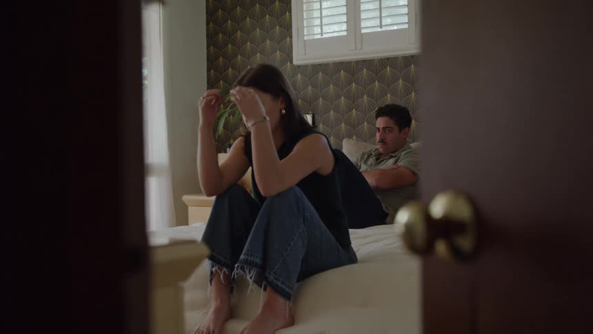 Woman sitting with hands on her head while man watches in the background