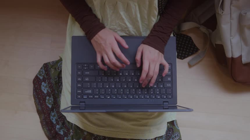 Woman sitting down typing on a laptop computer in her lap