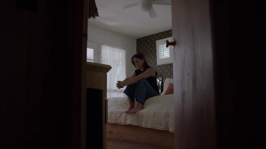 A woman sadly sits on the bed