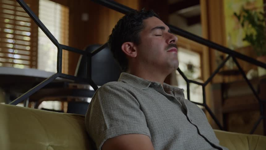 Man leans back on the sofa with eyes closed in a calm environment