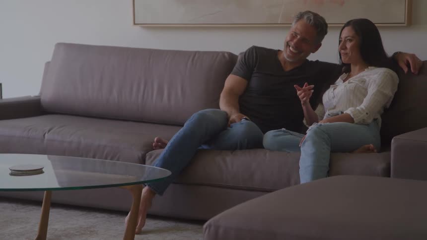 Couple sitting on the couch laughs while talking in a bright living room