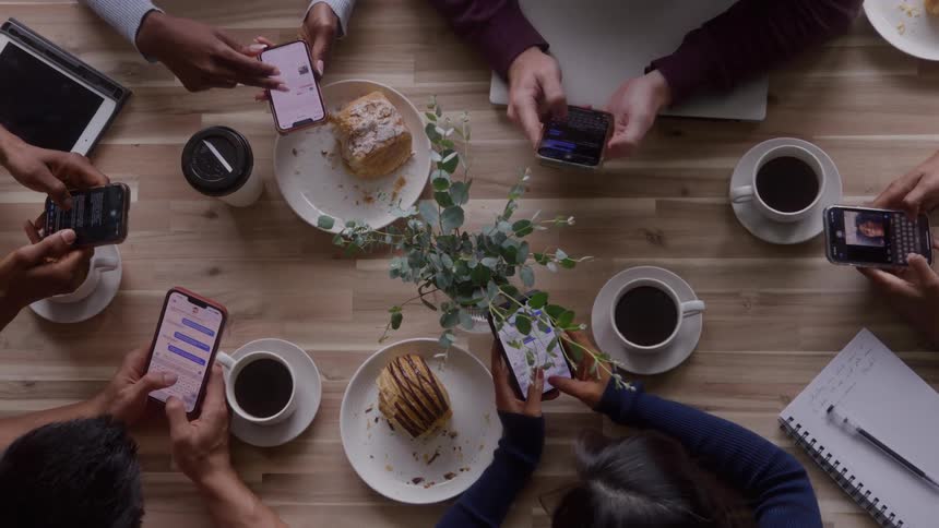 A group of friends using their mobile phones while sitting together at a table in a cafe during daytime