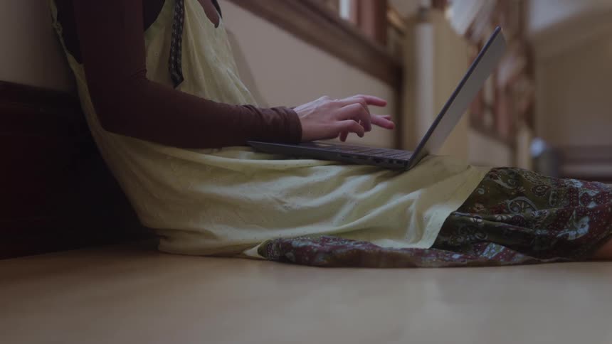 A young woman using a laptop computer while sitting on the floor in a room during daytime