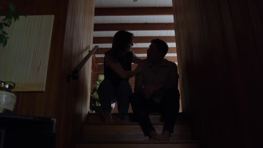Woman sits next to her husband on the wooden stairs exchanging close glances
