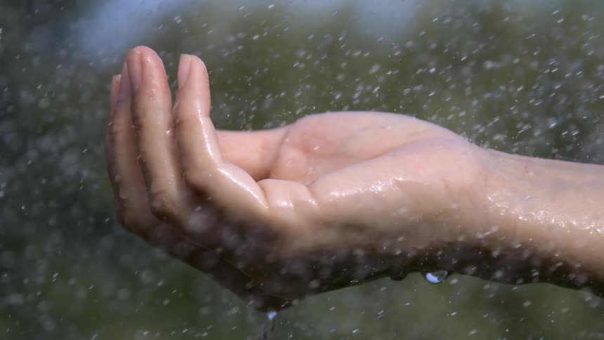 Close up of a persons hand outdoors under sprinkling water during daytime
