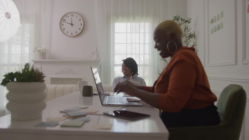 Two young black women conversing while working together in an office during daytime