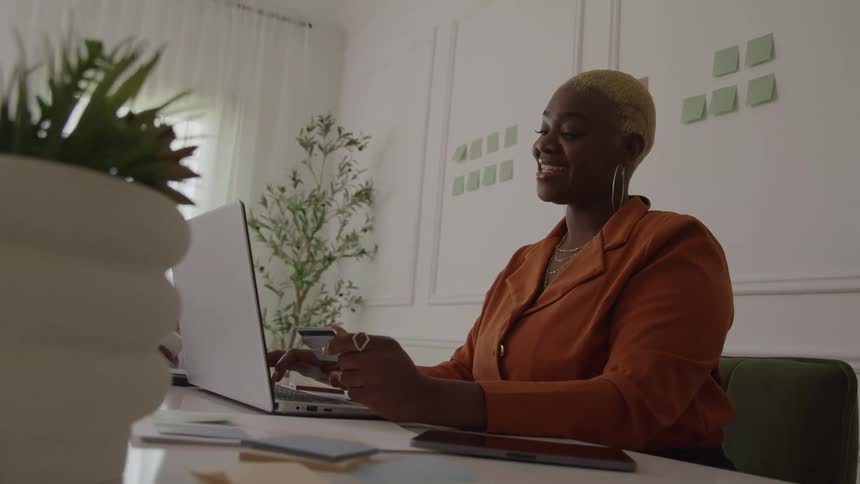 A young black woman working with a laptop computer while sitting at a table in an office during daytime