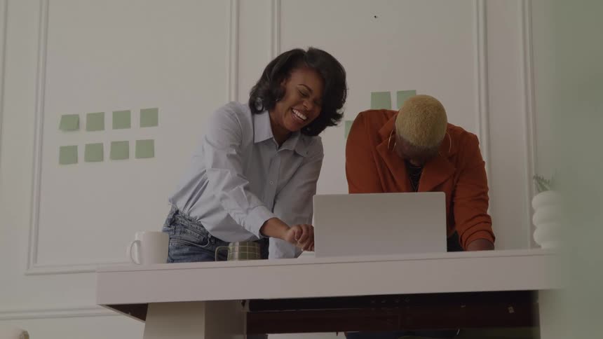 Coworkers smiling while working together on a laptop over the desk
