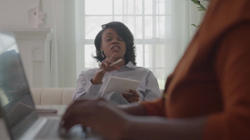 Two young black women conversing while working together in an office room during daytime