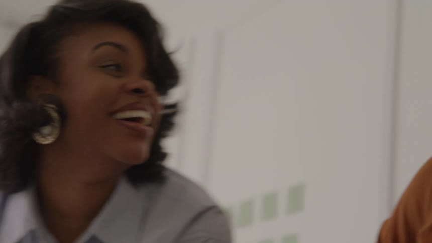 Two women smile together during a lively conversation in a work setting