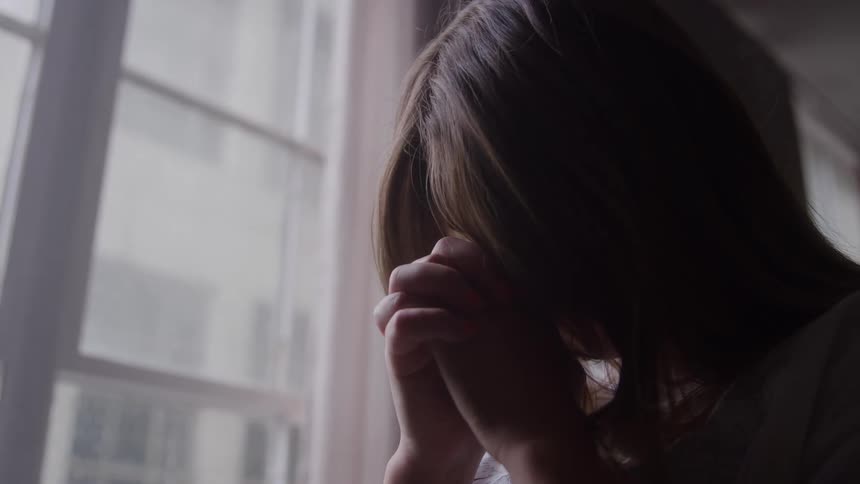 Woman sitting near the window rests her head in her hands in a moment of reflection