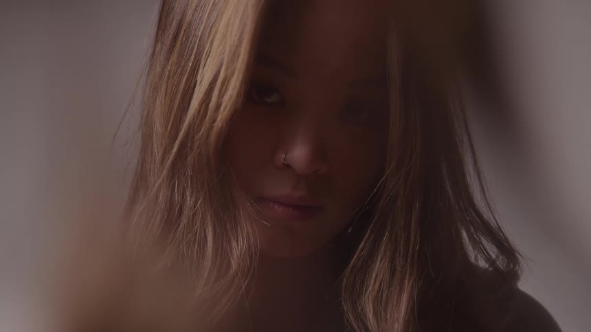 A young woman with long blonde hair stands indoors after styling her hair admiring the finished look