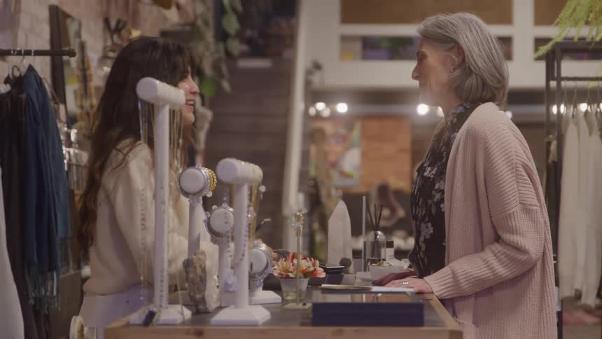 Grayhaired woman smiling while talking with a shop attendant in an accessory store