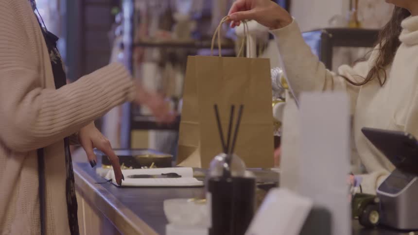 Clerk hands a paper bag to the customer at the store counter