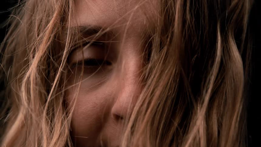A young woman with long blonde hair looks sad as the wind gently blows through her hair