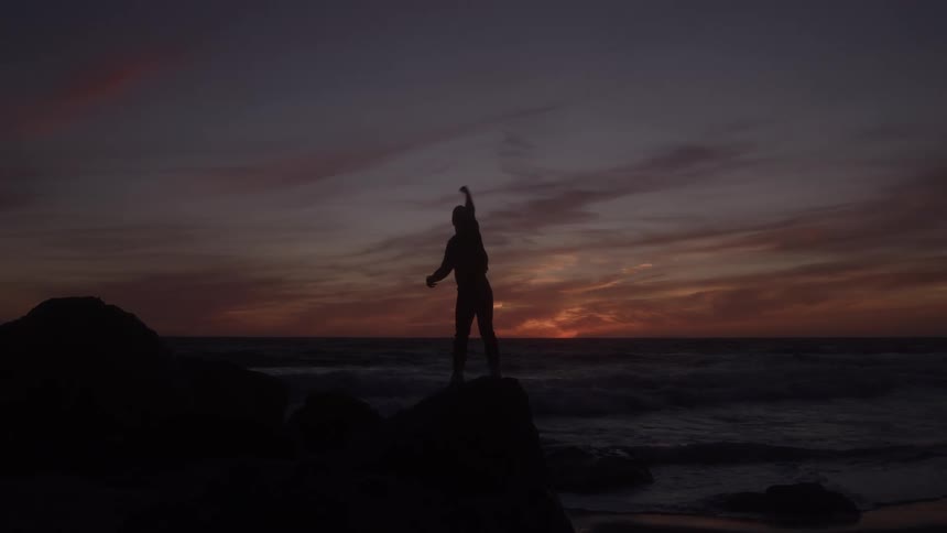 Silhouette raising an arm before the ocean sunset