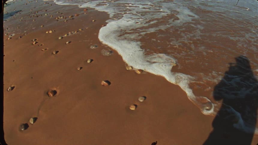 Sea foam moves over the sand scattered with small stones