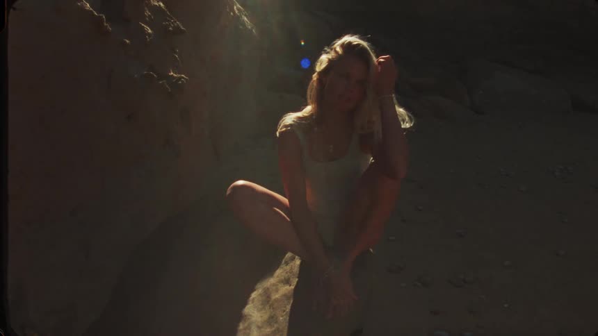 Woman sits on a rock lit by a beam of light amid shadows on the beach