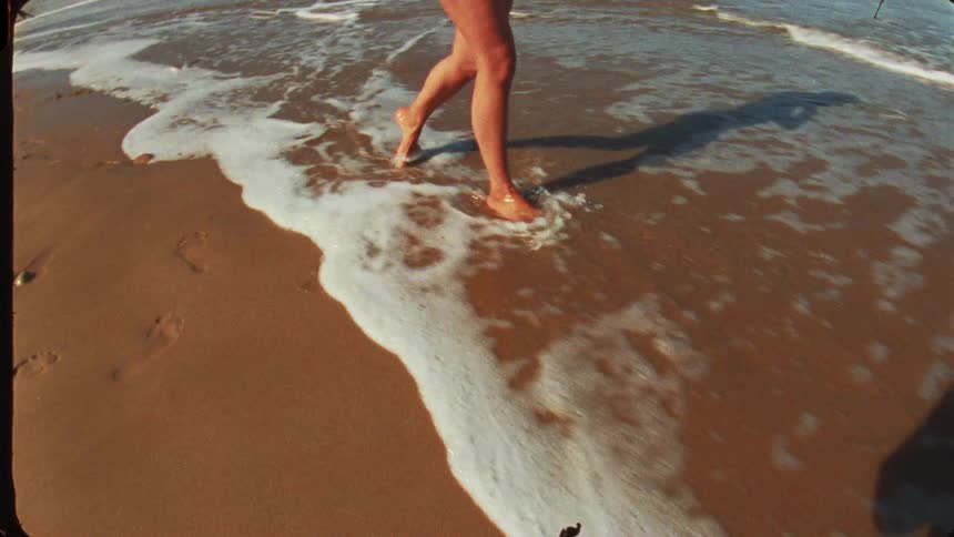 Woman walks along the shore leaving footprints on the wet sand