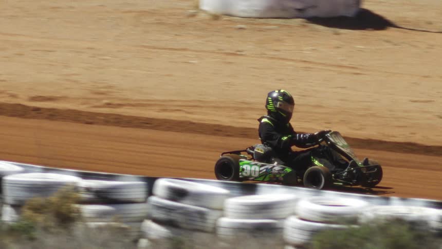 This is a closeup shot of an exciting race as several gokarts speed around a corner on the dirt trackthe lead kart numbered 30 and primarily black and green passes close to a barrier made of stacked white tires in the foreground