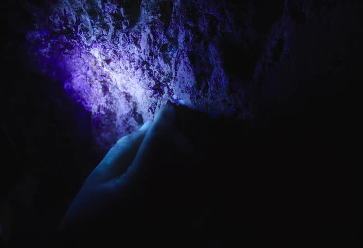 The person picks at the rocks of the cave wall