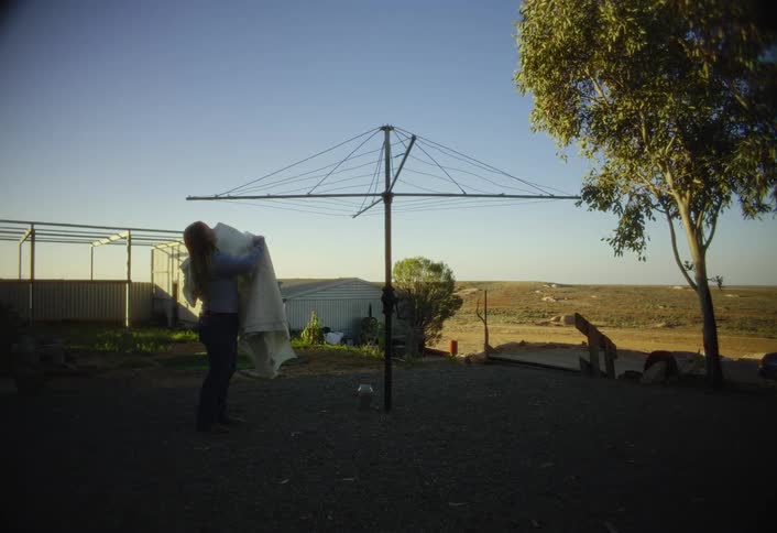 Woman hanging clothes on an outdoor clothesline at sunset