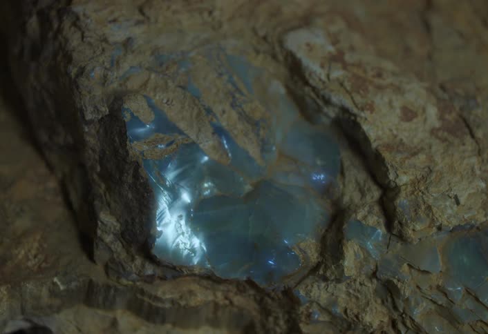 A glowing blue crystal is embedded in rough brown rock