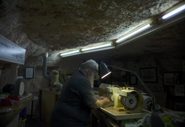 An older man works at a grinding machine in a dim underground workshop