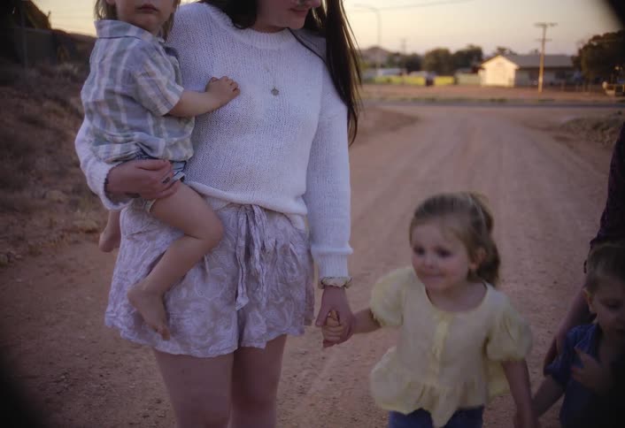 Woman walks along a dirt road holding one child in her arms and another by the hand