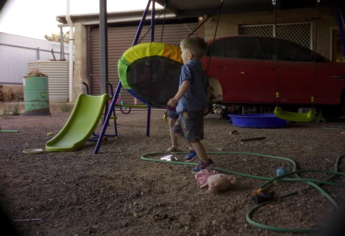 Children play on a swing and slide in a yard with a car in the background