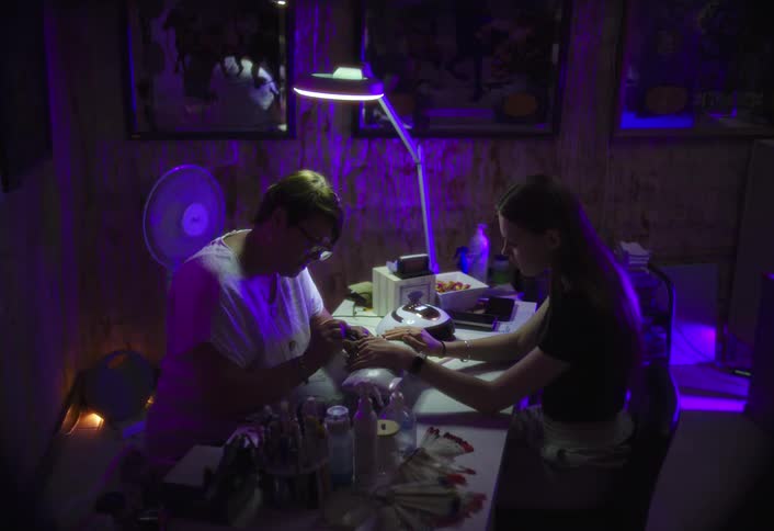 Woman holds her hand out allowing a professional manicurist to paint her fingernails