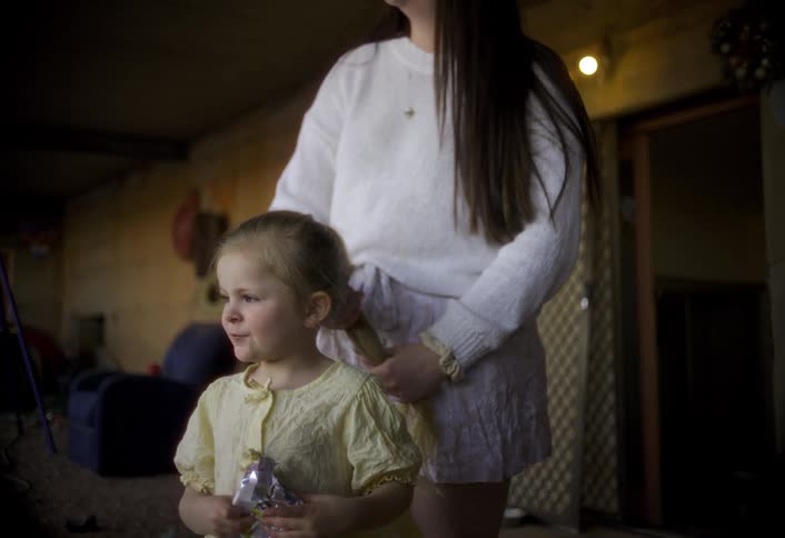 The girl eats candy as her sister brushes her hair