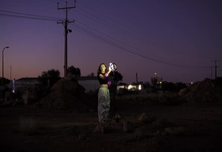 Woman adjusts the lighting of a ring light in an open area at dusk