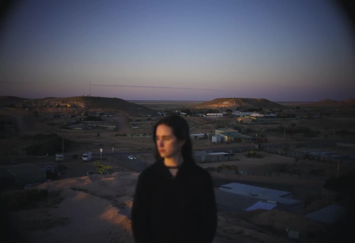 A person stands silhouetted against a quiet desert town at dusk
