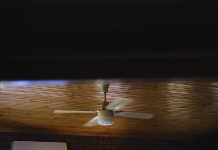 Pale ceiling fan hanging from a wooden ceiling operates in a large room during the daytime