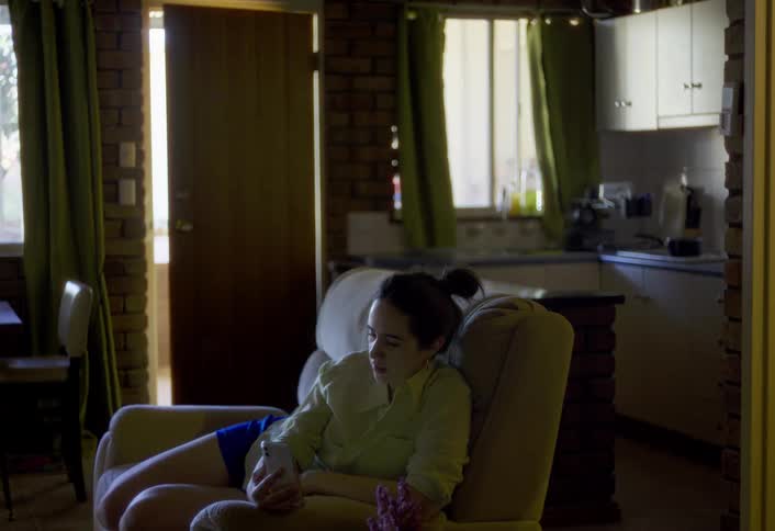A woman sits in an armchair video calls in a dimly lit living room