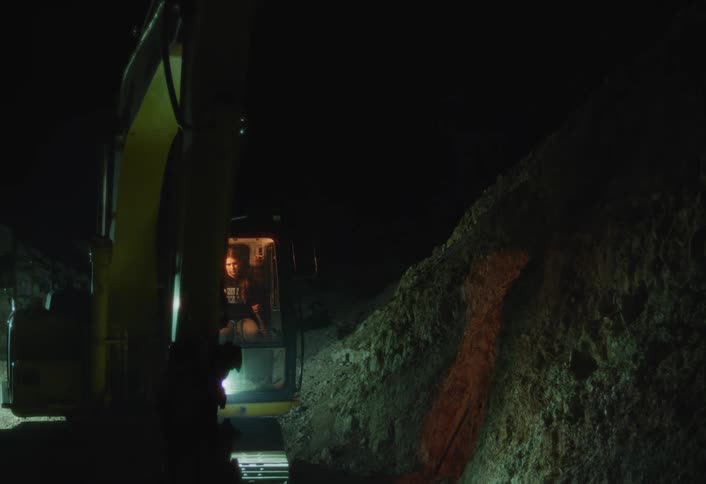 Person operating an excavator at night with the front light on