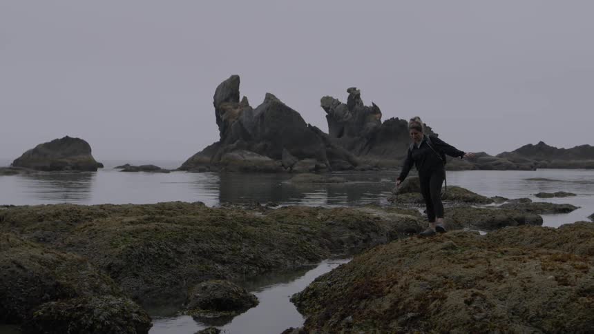 A woman walks on the rocky coast