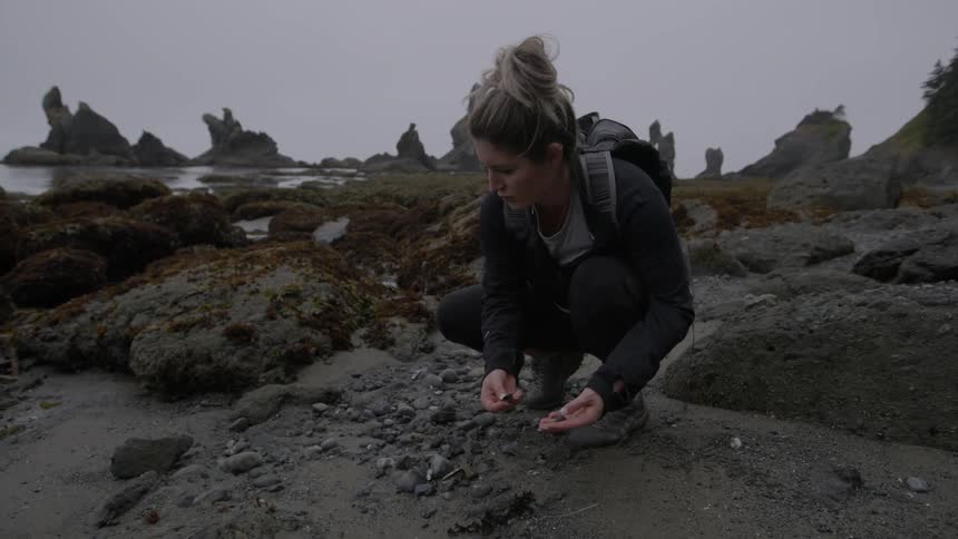 A woman is picking up pebbles by the shore