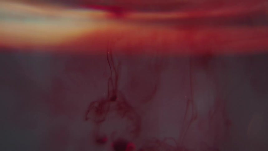 A droplet of red viscous liquid drops into water