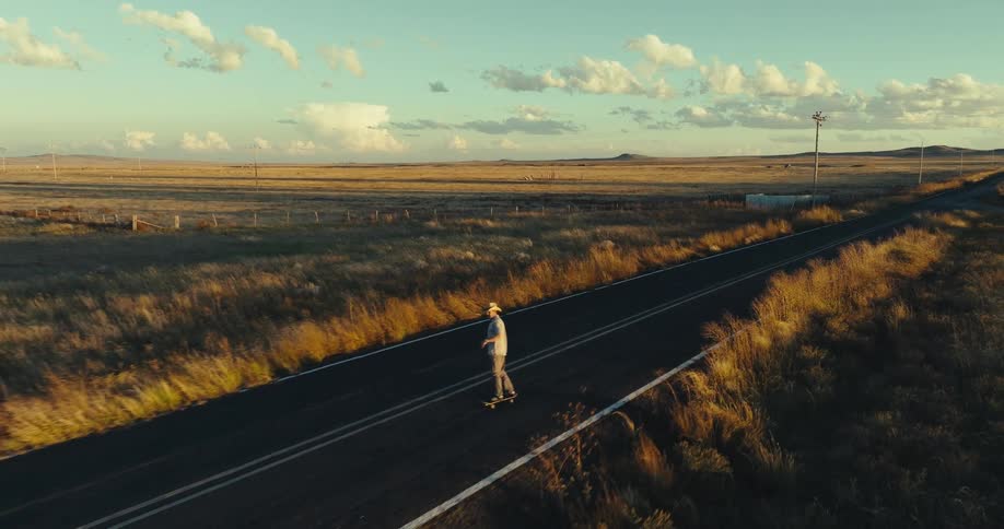 A white male is skateboarding down the center of a rural highway
