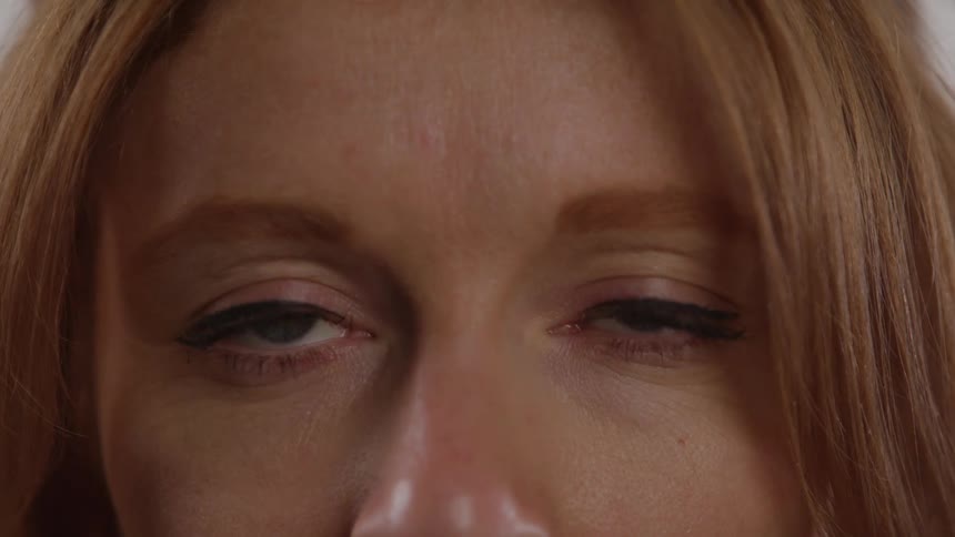 The video is an extreme closeup focusing intensely on the eyes and upper face of a person with reddishblonde hair the person has striking bluegreen irises and welldefined eyelashes and they blink once before maintaining a steady gaze toward the came