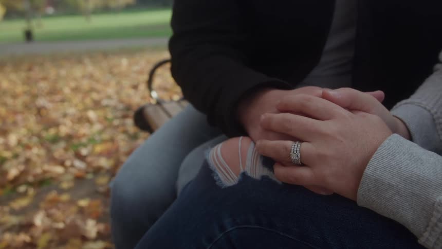 Couple holding hands while sitting on a bench surrounded by autumn leaves