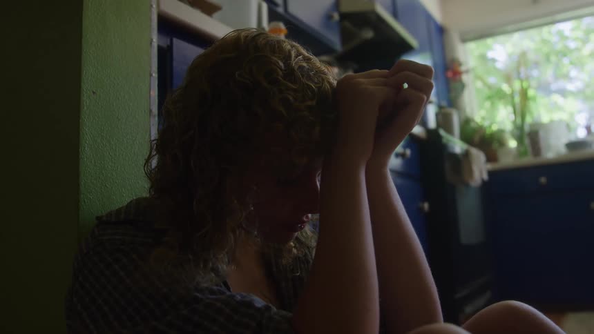 Close up of a young woman sitting contemplatively indoors on the kitchen floor during daytime