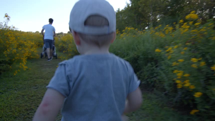 The boy is chasing after his father past the flowers