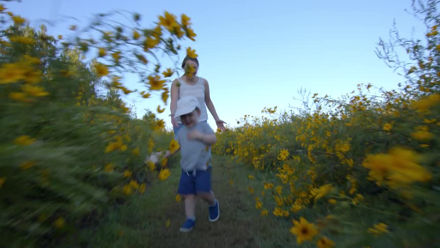 Mother and son walking playfully through a path in a flower field during daytime