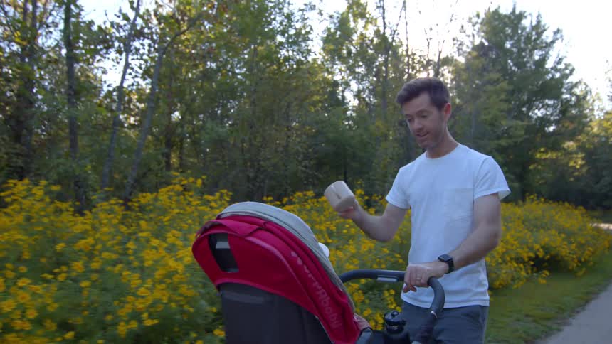 Young man pushing a baby stroller while laughing in a road surrounded by trees and vegetation outdoors during day time