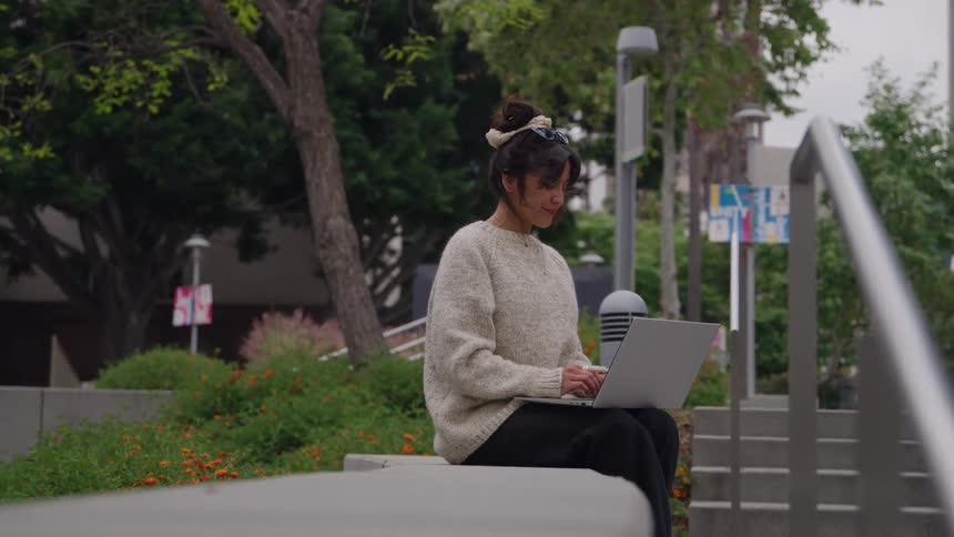 A woman works on her laptop while sitting in the city park