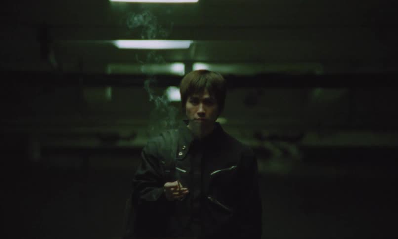 A young asian male smoking while standing at a terminal at night