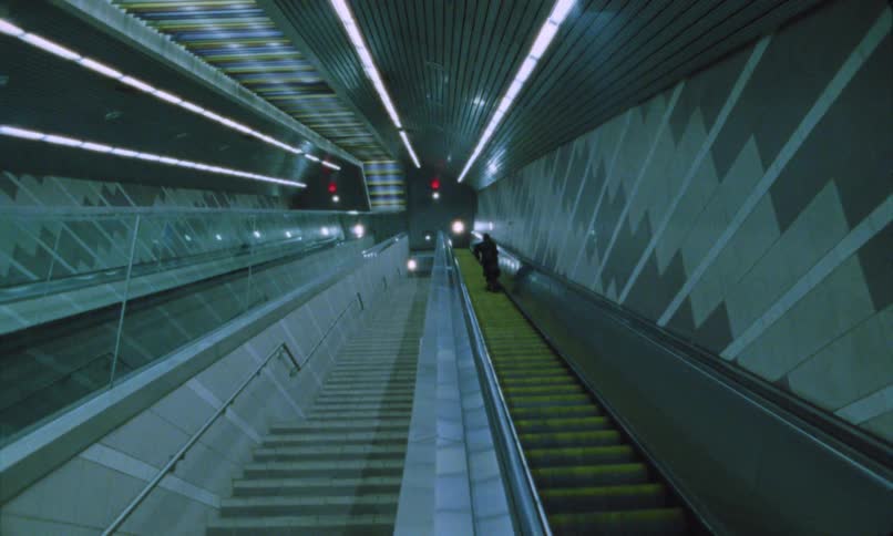 A person rides up an escalator inside a modern underground station